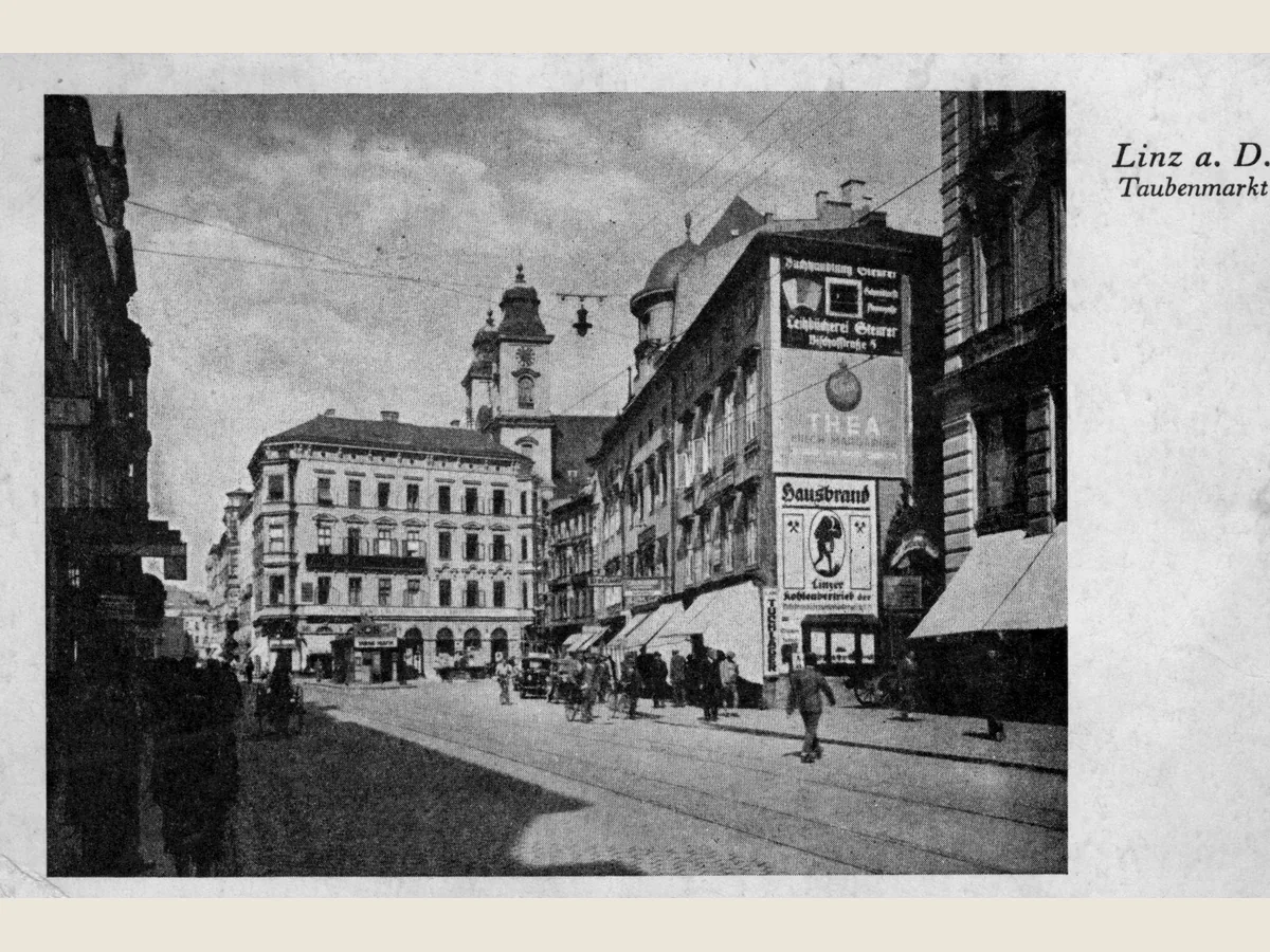 Historische Schwarz-Weiß-Postkarte des Taubenmarkts in Linz mit Straßenbahn, Passanten und Häusern der Landstraße, 1935